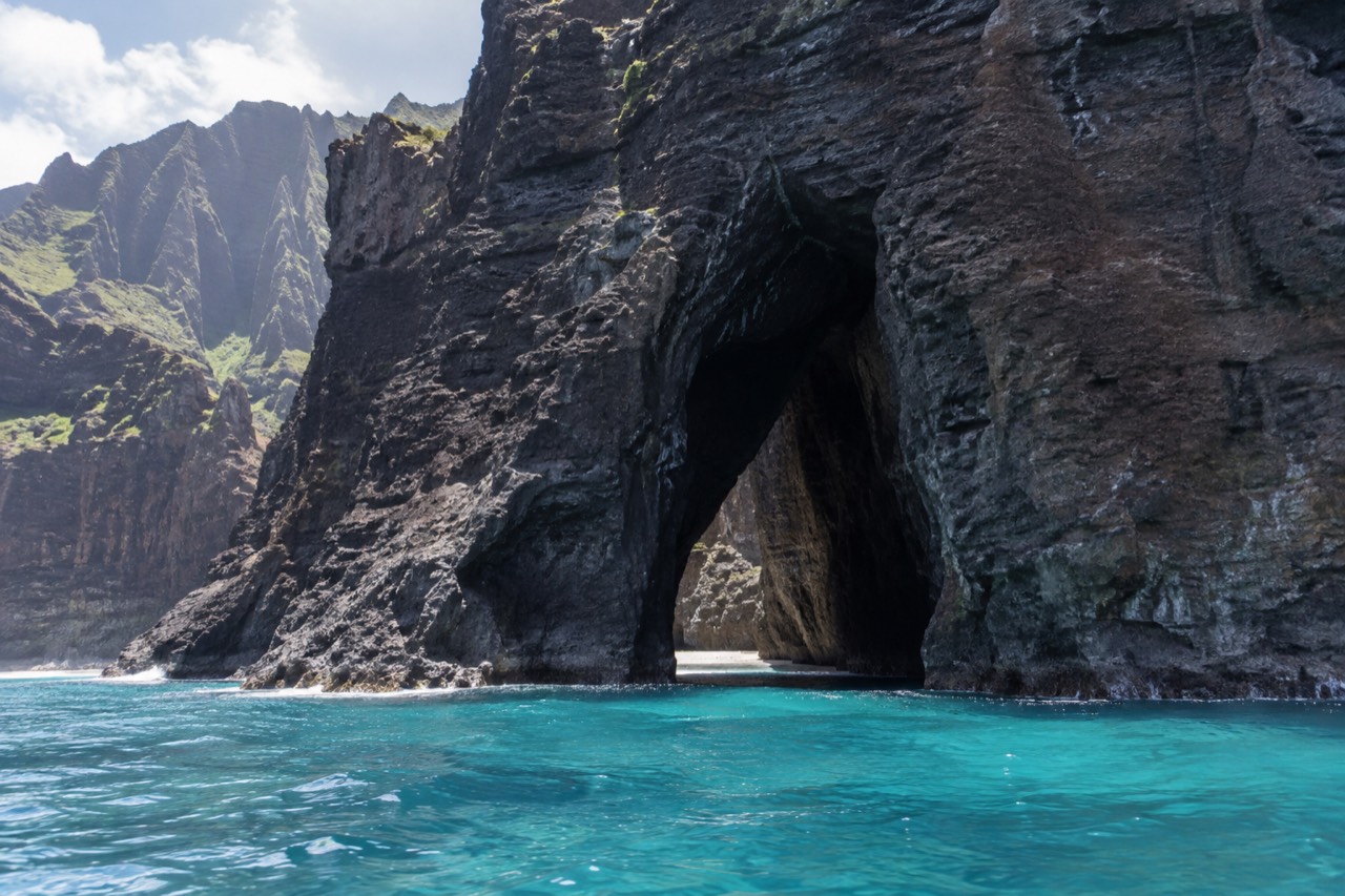 Sea cave opening in a cliff face along a tropical coastline with blue ocean water inside