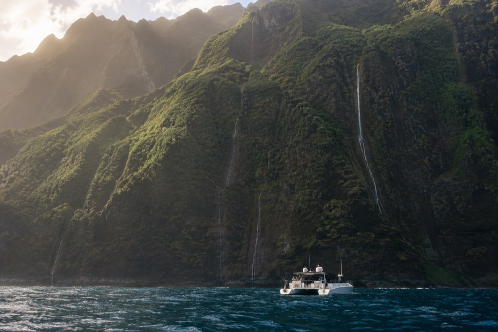 Power catamaran cruising close to green sea cliffs on the Napali Coast