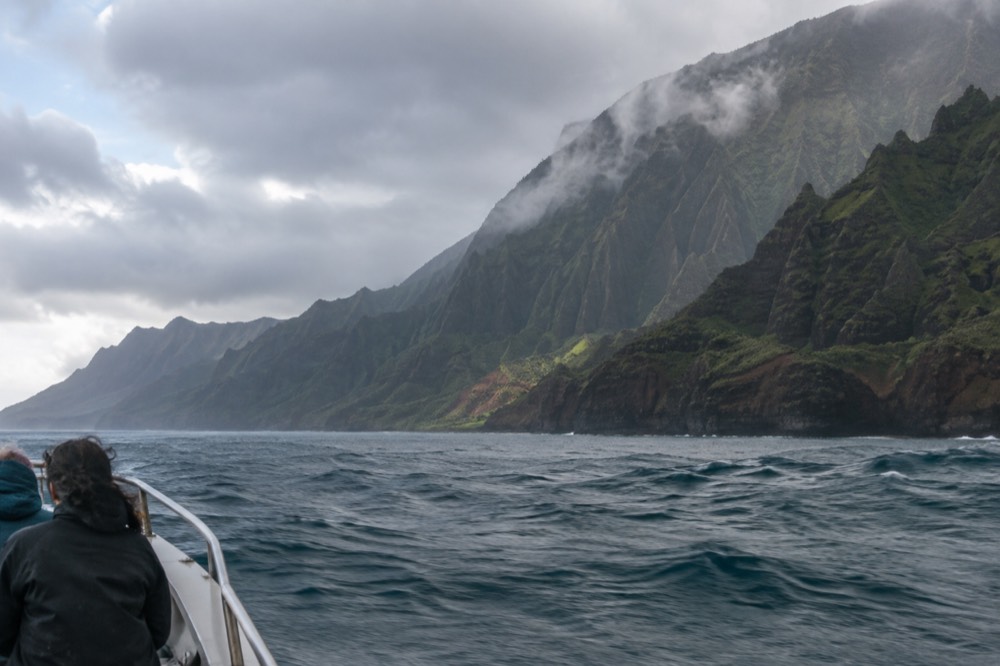 Green Napali cliffs meeting calm blue ocean beneath scattered clouds