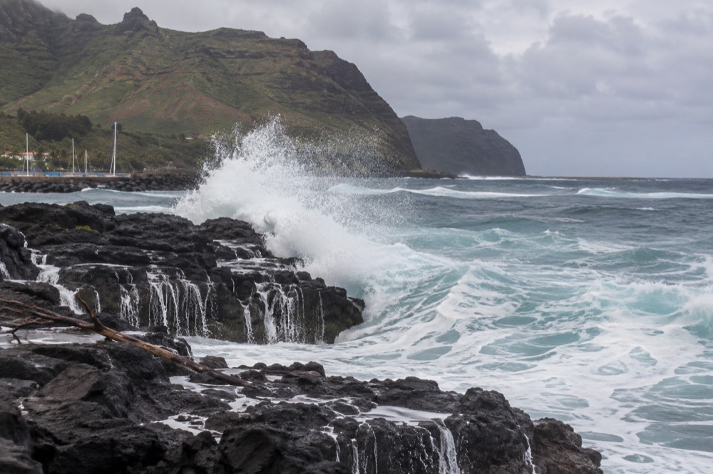 Large ocean swells rolling toward a dark volcanic coastline under a cloudy winter sky