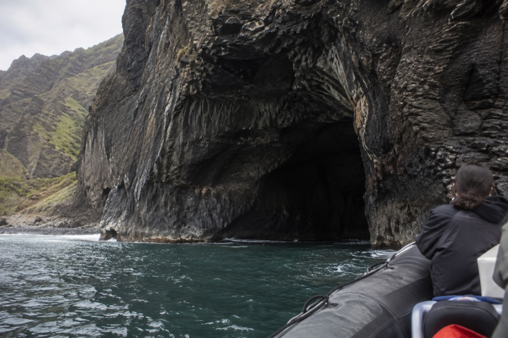 A low rigid hull raft holding position near the dark mouth of a sea cave in a cliff face
