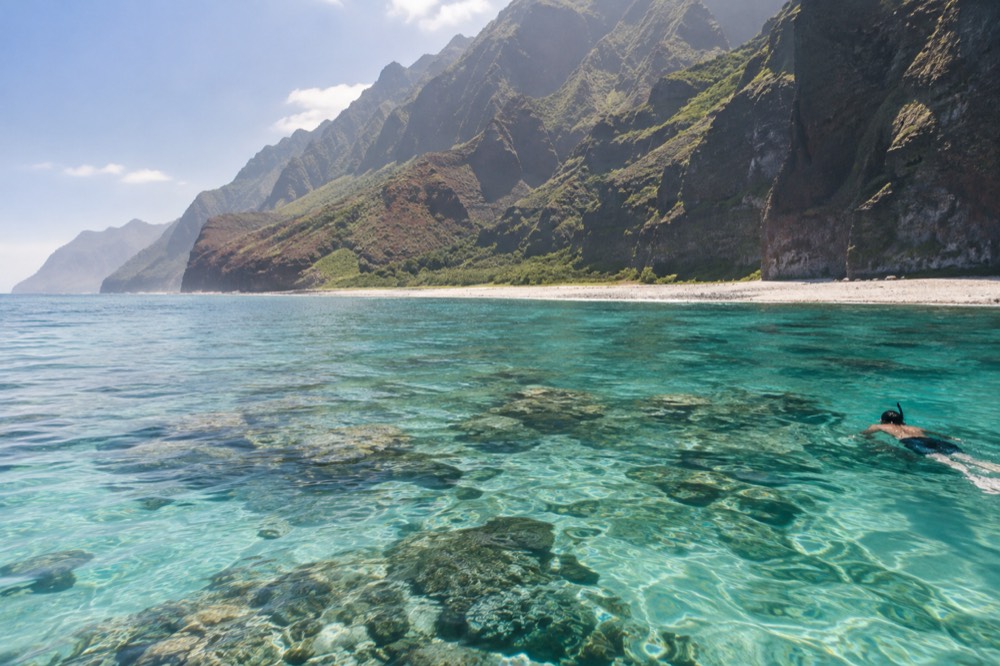 Calm turquoise water over a shallow coral reef near the base of sea cliffs