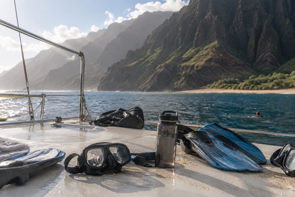 Snorkel masks and fins arranged on the deck of a boat moored near a Napali Coast reef.