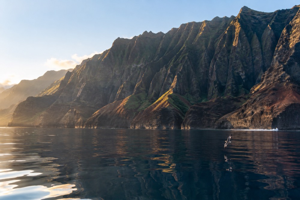 Glassy early morning water off the Napali Coast with sea cliffs rising from a calm sea