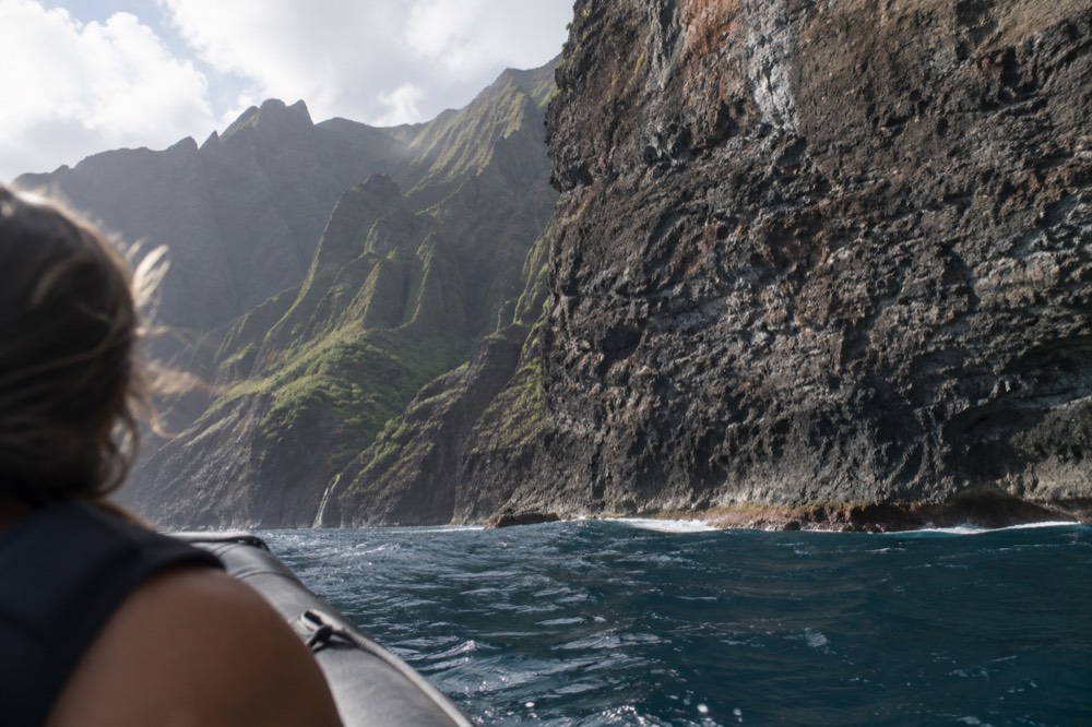 A rigid inflatable raft cruising close to green sea cliffs on the Napali Coast