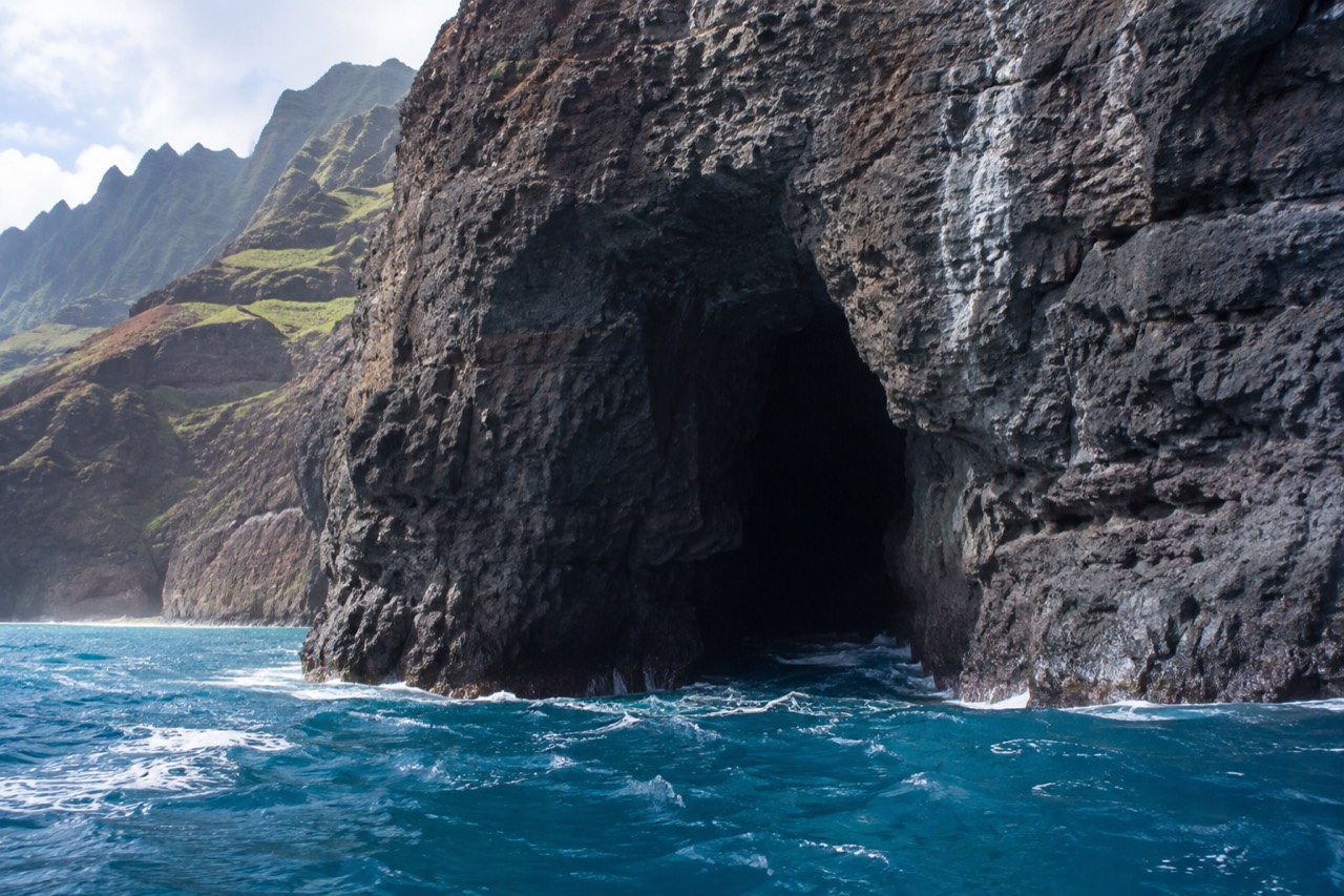 A dark sea cave opening in a cliff face above calm blue water