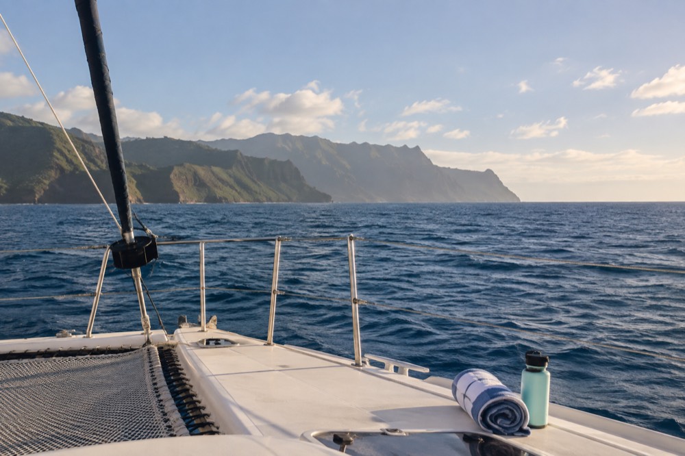 A calm boat deck on open blue water near distant cliffs