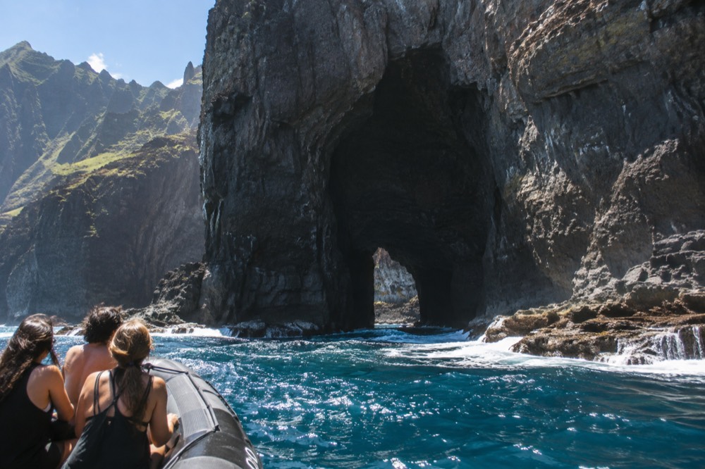 A small rigid inflatable boat passing a dark sea cave entrance in a cliff face