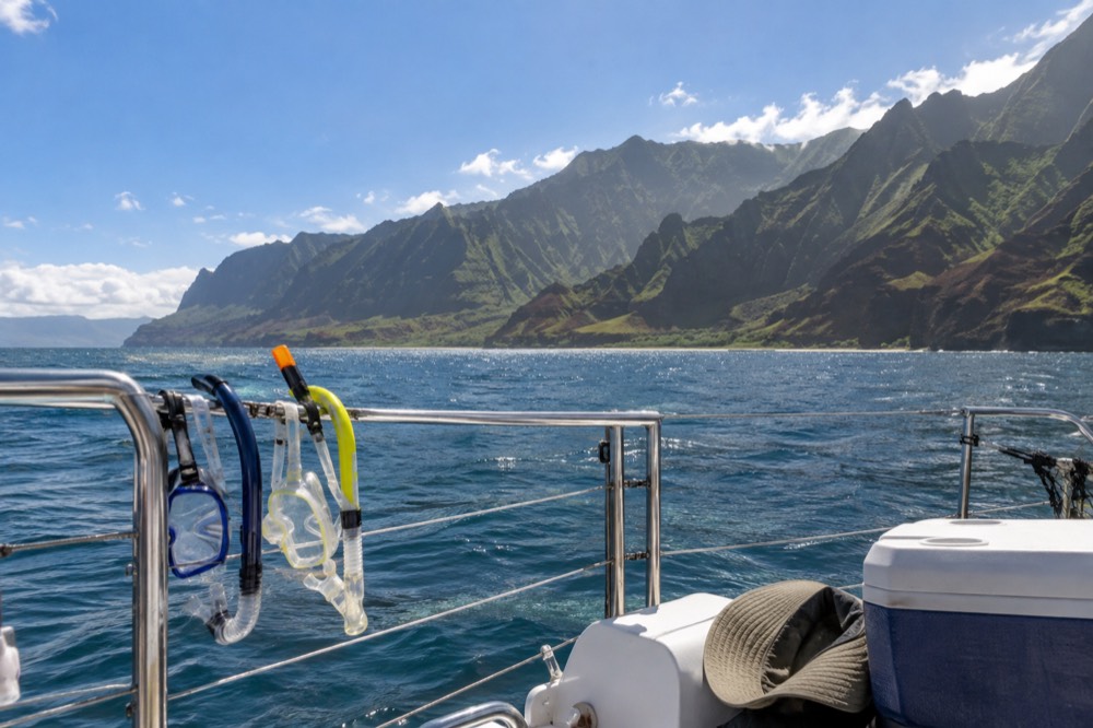 A catamaran deck viewed from the stern with green Napali cliffs across the water