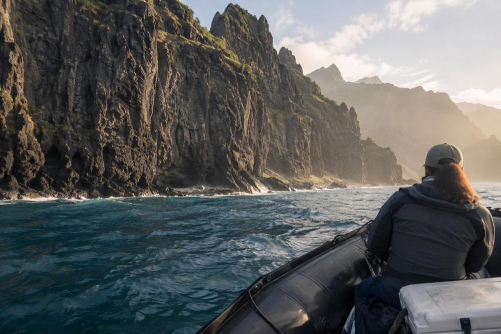 A rigid inflatable raft cruising close to tall fluted sea cliffs along a remote coastline.