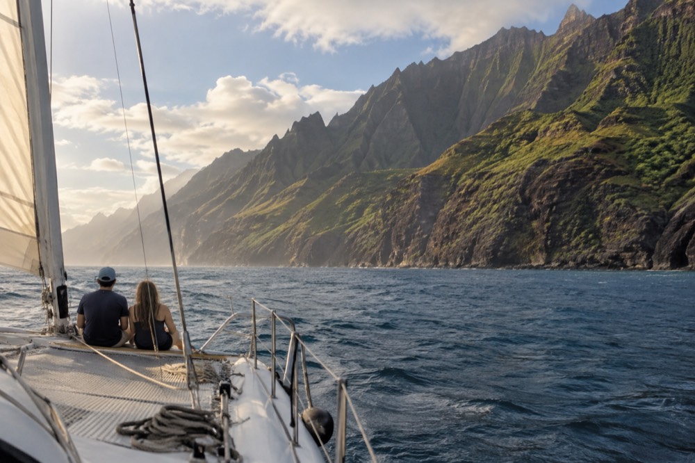 A catamaran sailing along green sea cliffs on a calm afternoon near the Napali Coast