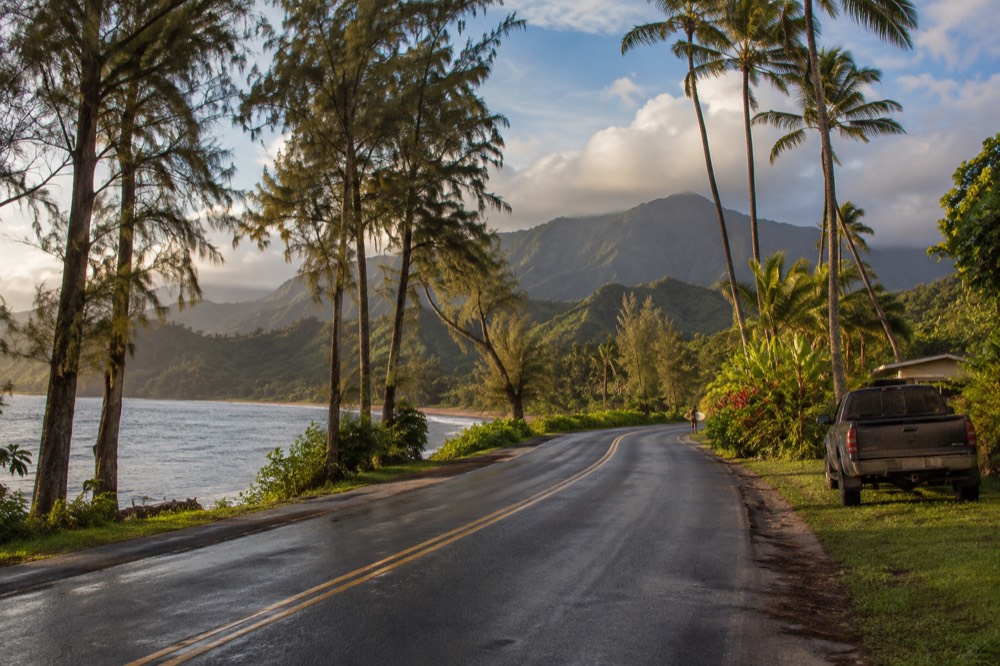 A winding coastal road with green mountains and ocean views along Kauai's north shore