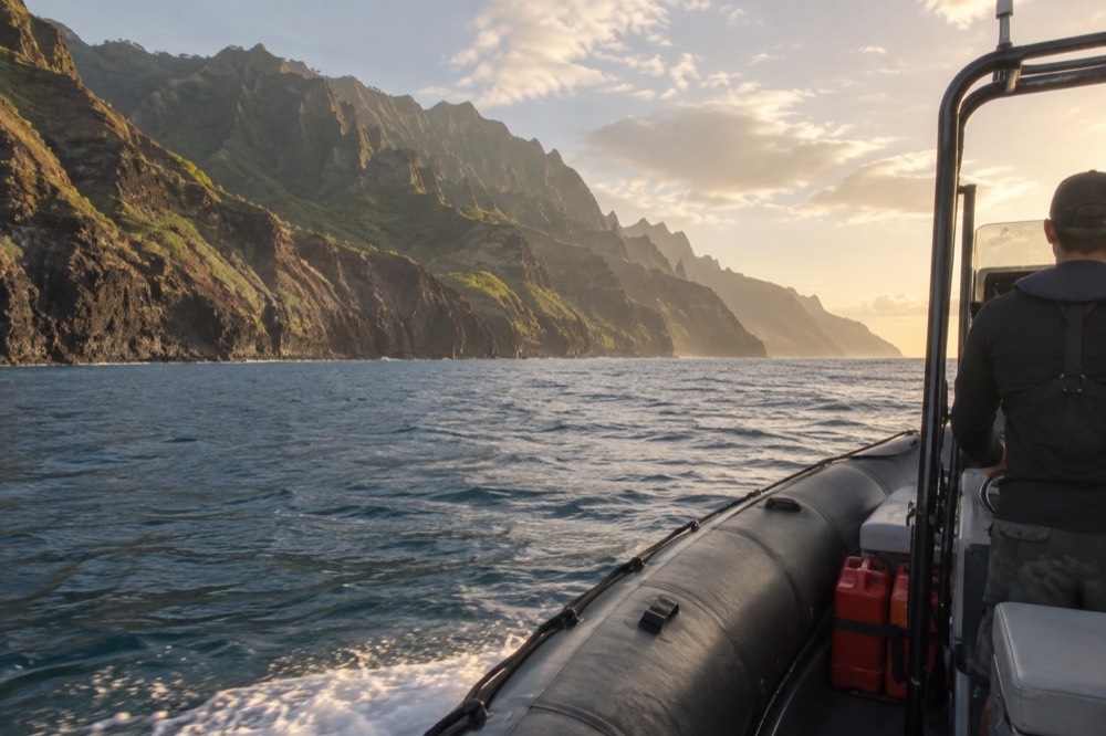 A rigid hull inflatable raft running parallel to tall fluted sea cliffs along the Napali Coast