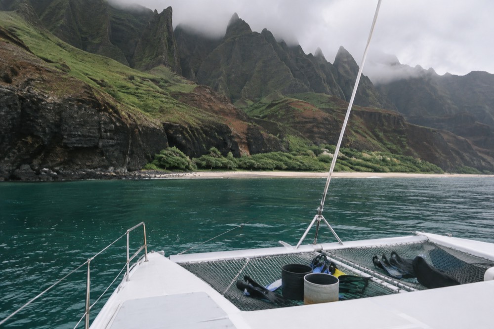 A power catamaran anchored in clear water near the Napali Coast with passengers preparing to snorkel