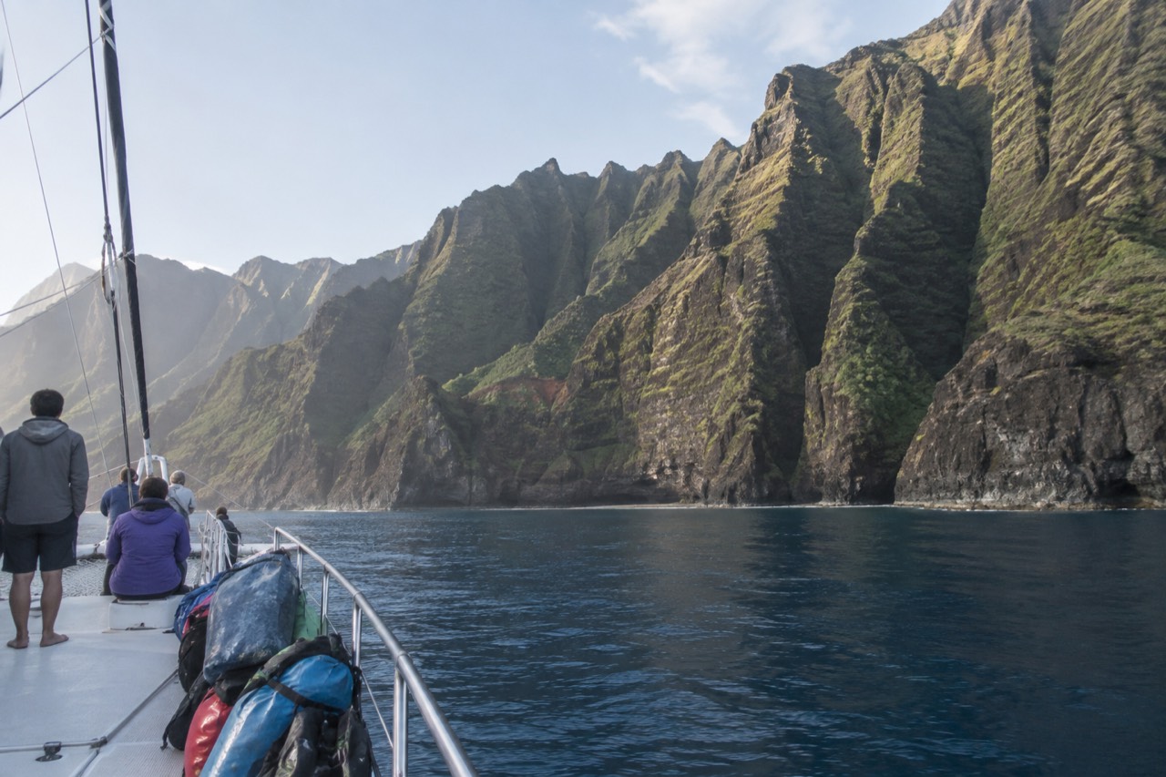 A catamaran cruising close to the green sea cliffs of the Napali Coast on calm water