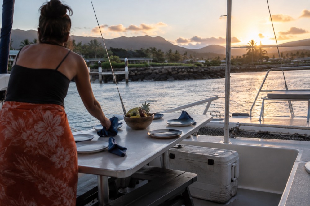 A crew member setting a dinner table on the deck of a catamaran before departure