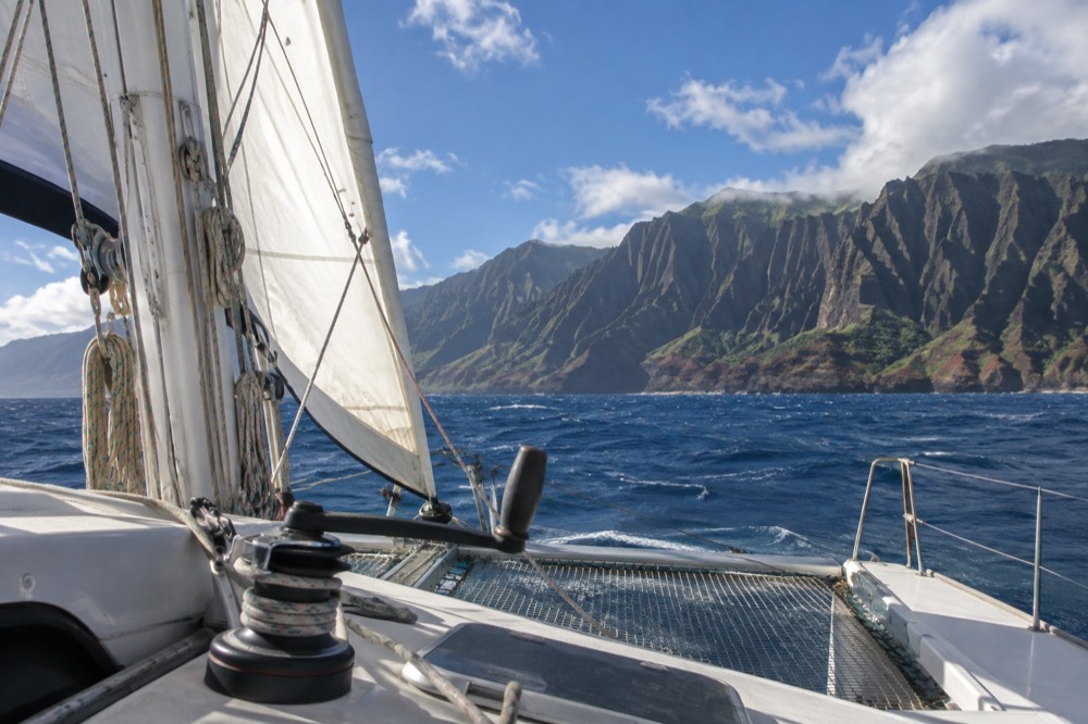 A sailing catamaran under full sail on open water between Kauai and the Napali cliffs