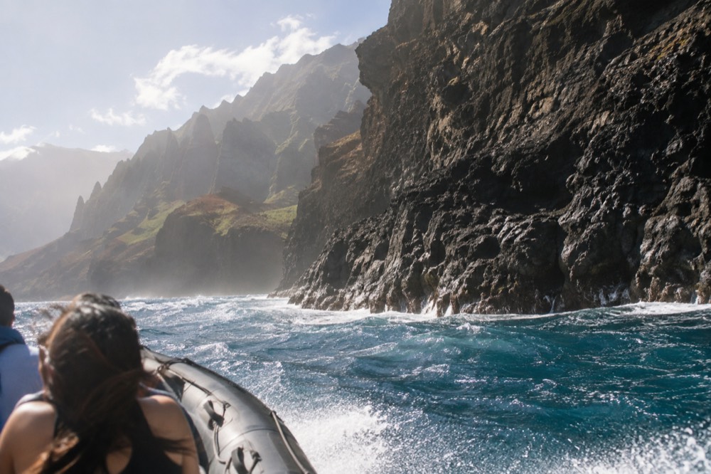 A rigid-hull inflatable raft running close to the base of the Napali sea cliffs