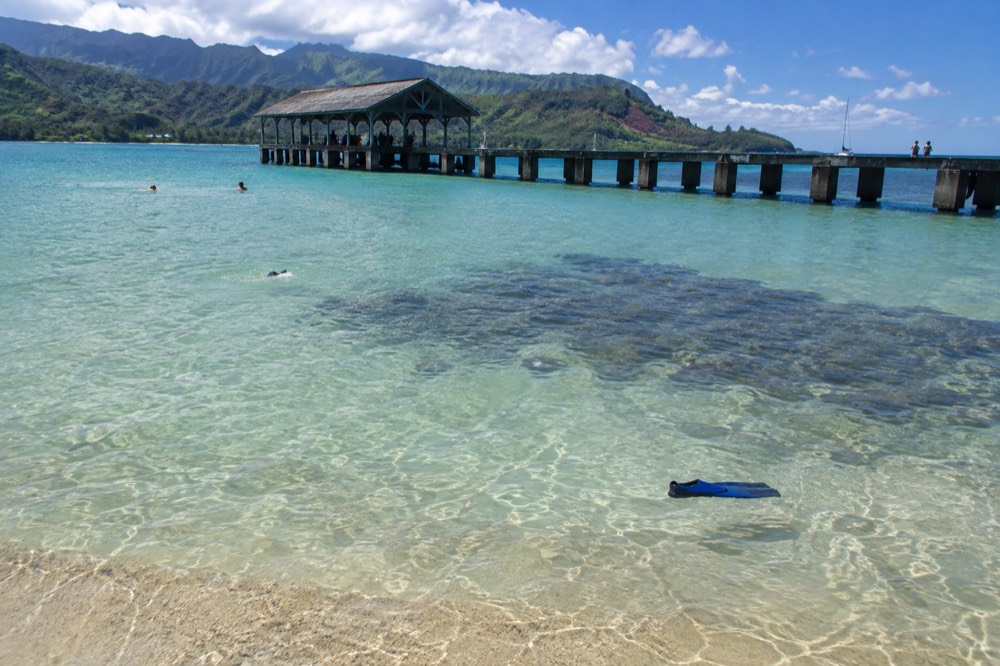 A calm turquoise bay with a long pier reaching over shallow water