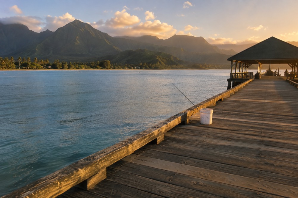 The weathered wooden Hanalei Pier reaches over shallow turquoise water at Hanalei Bay