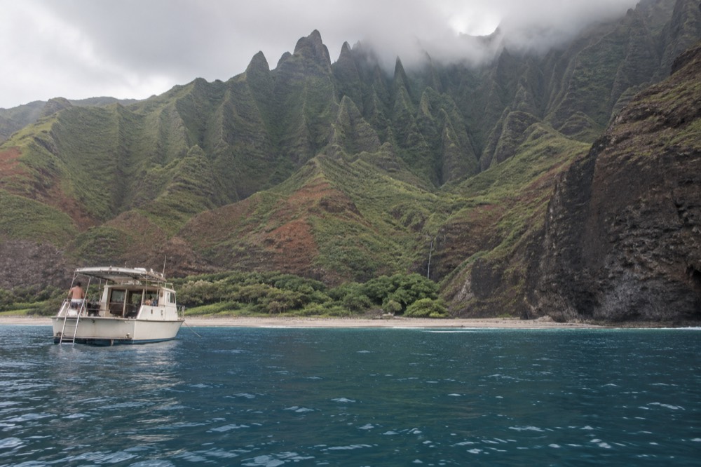 A small boat anchored in a quiet bay beneath steep green sea cliffs