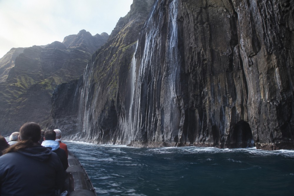 A rigid inflatable raft cruising close to tall sea cliffs along a green coastline