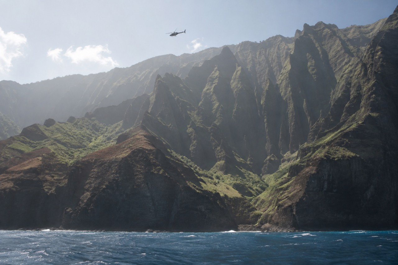 A helicopter flying over green sea cliffs along a tropical coastline