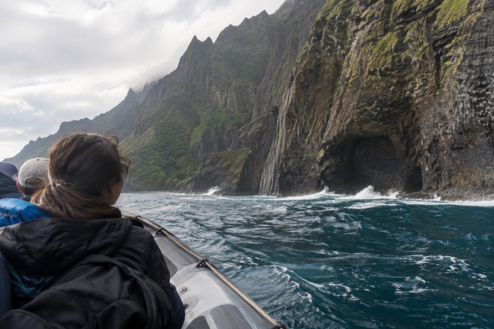 A rigid inflatable raft passing beneath tall green sea cliffs along the Napali Coast