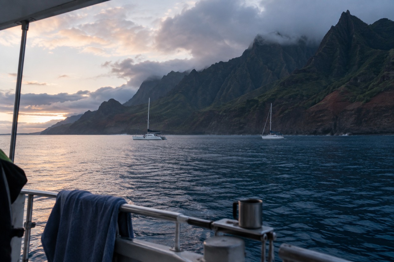 A calm anchorage on Kauai at first light with green cliffs rising behind moored boats