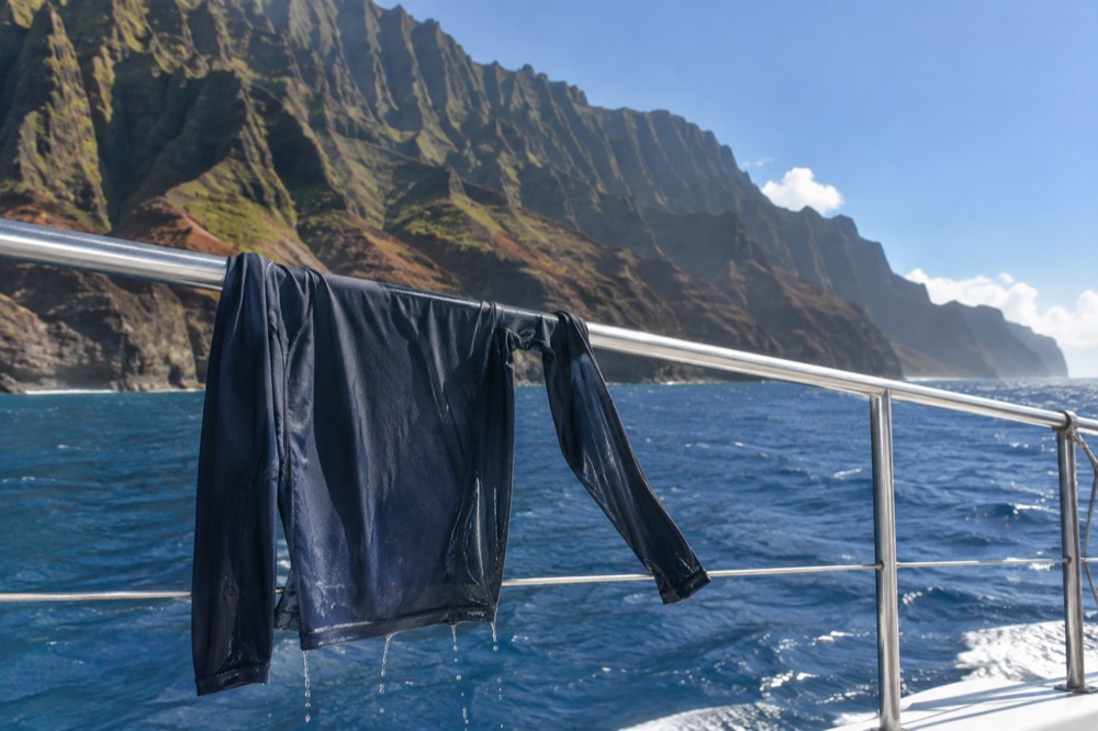 A dark long-sleeve rash guard drying on a boat rail under a bright tropical sky