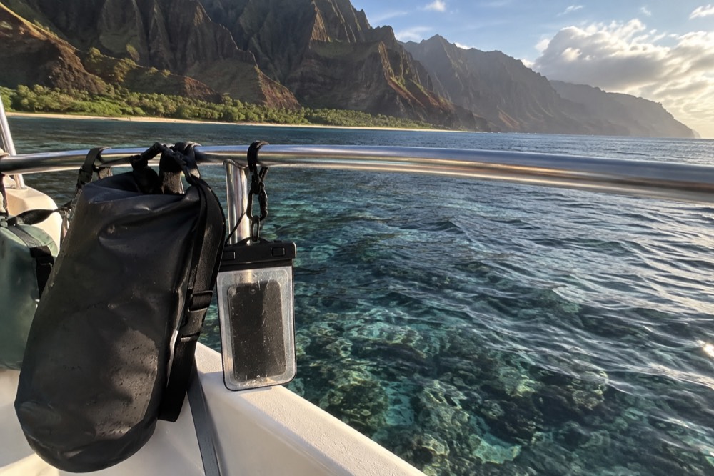 A dry bag and waterproof phone case clipped to a boat rail above clear reef water