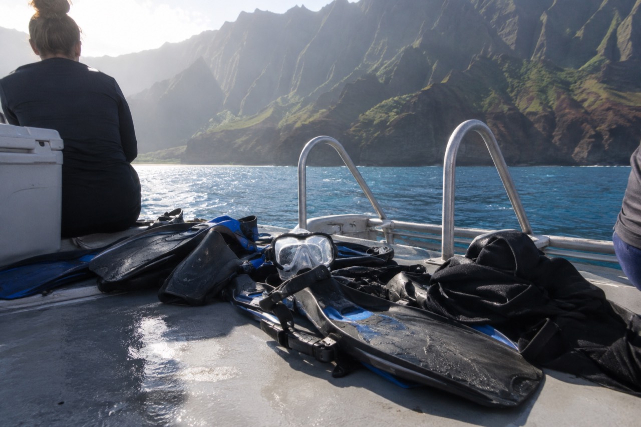 Snorkel gear and rash guards laid out on a boat deck near green Kauai cliffs