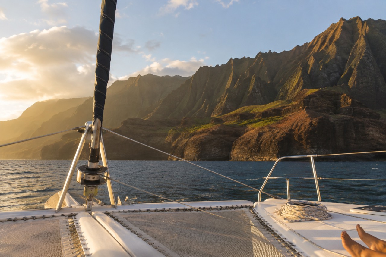 A catamaran under sail along the Napali Coast cliffs in golden evening light