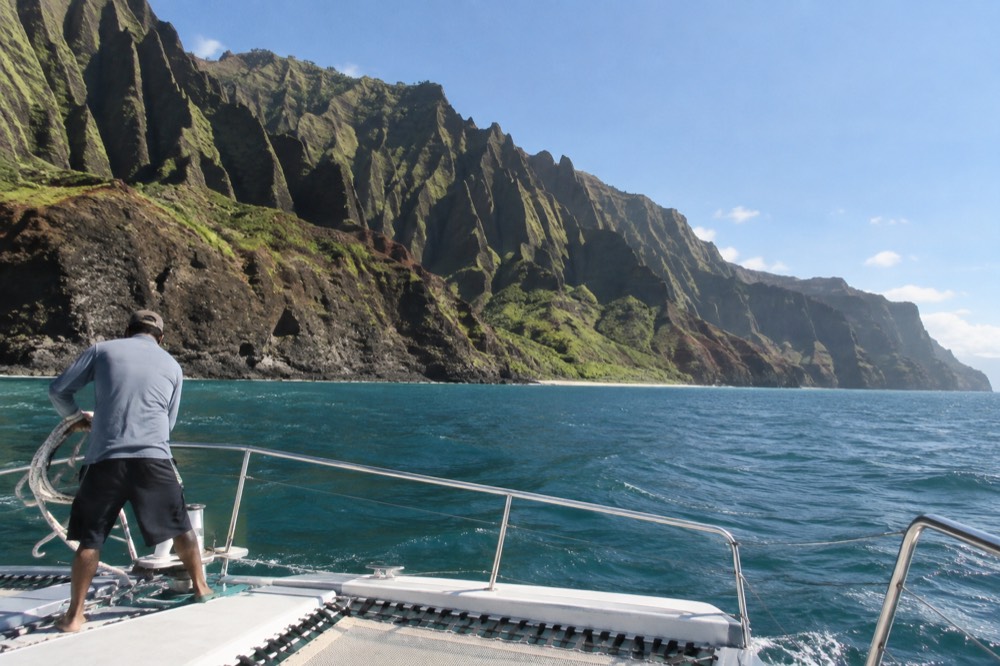 A power catamaran cruising past the Napali cliffs under a clear sky