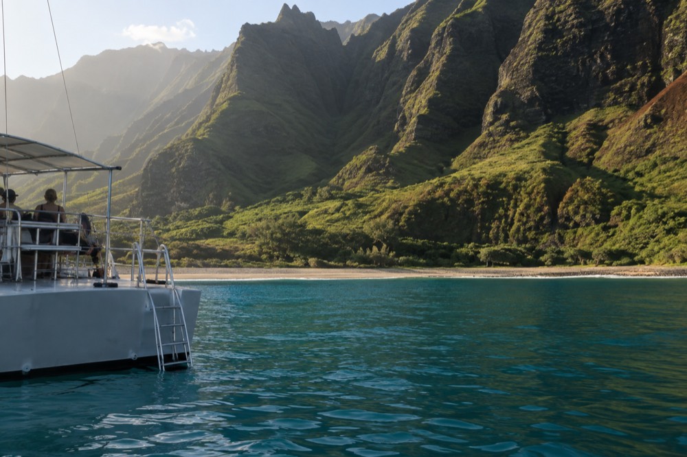 A calm turquoise bay with a tour boat at anchor near a green coastline