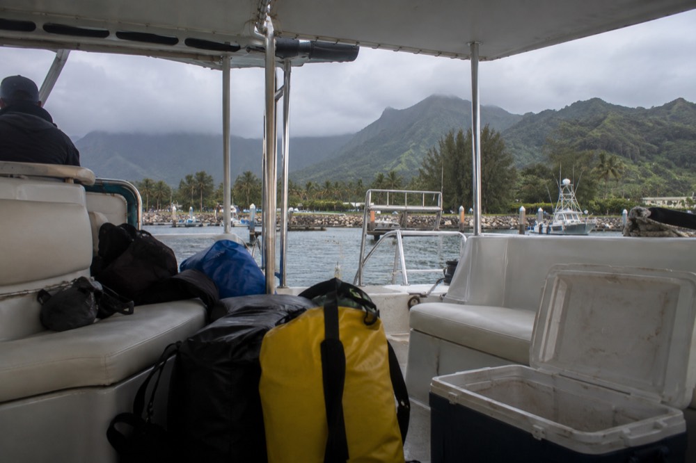 A catamaran cabin with padded seats and a rack of dry bags near the shaded seating area
