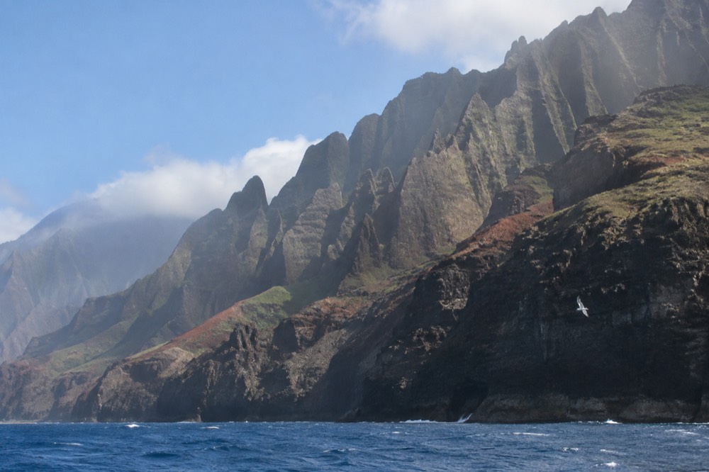 Jagged green cliffs of the Napali Coast rising from the ocean under a blue sky