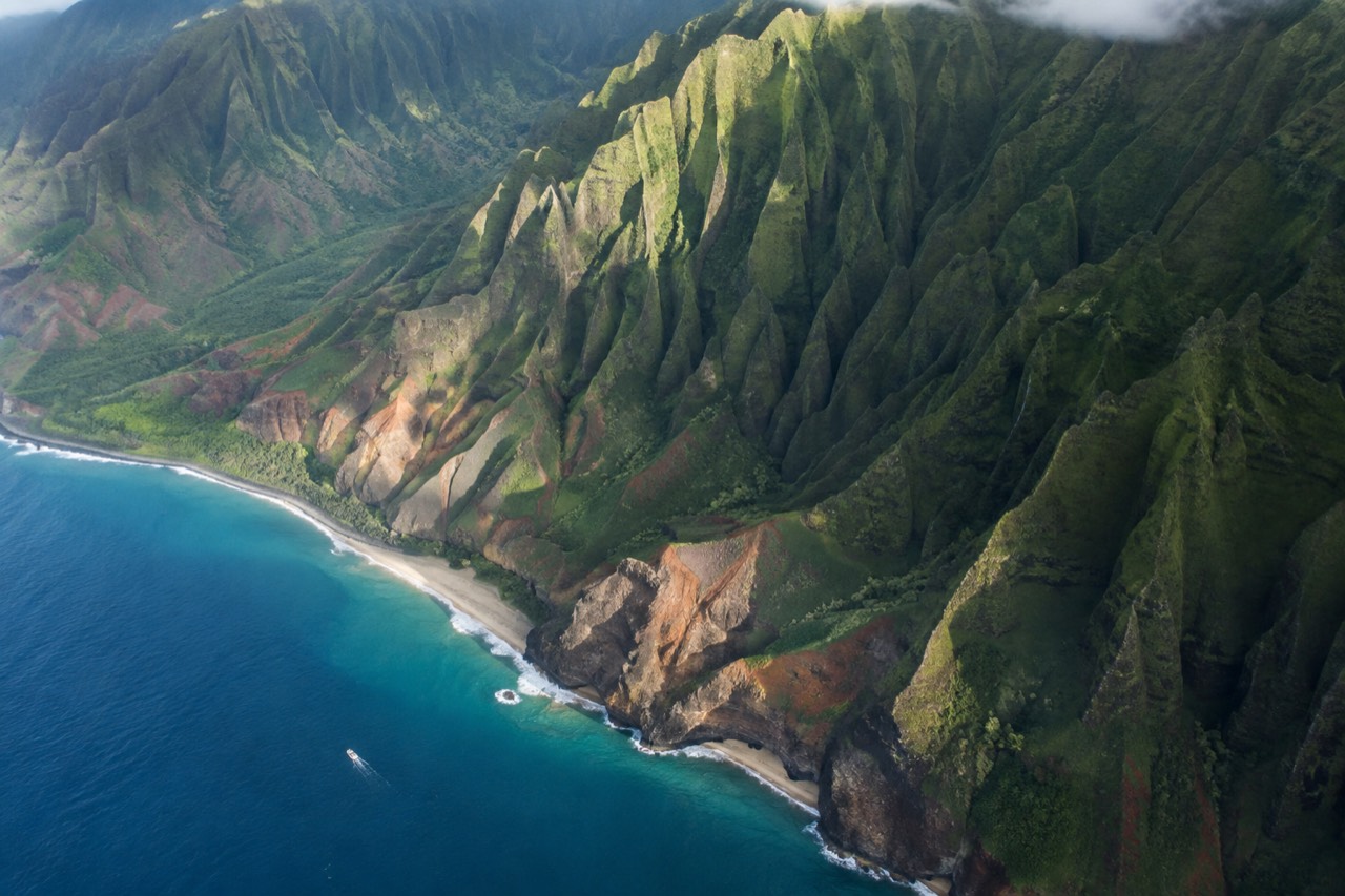 Aerial view of the Napali Coast with lush green cliffs and deep valleys meeting the blue ocean.