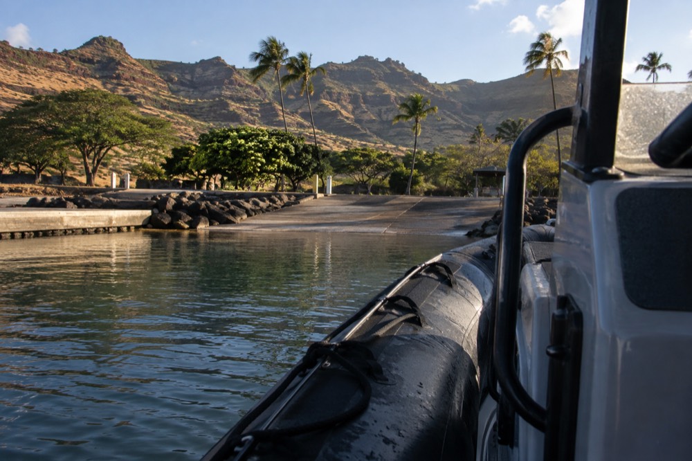 A rigid-hull inflatable raft cruising close to the sea cliffs of the Napali Coast on calm water.