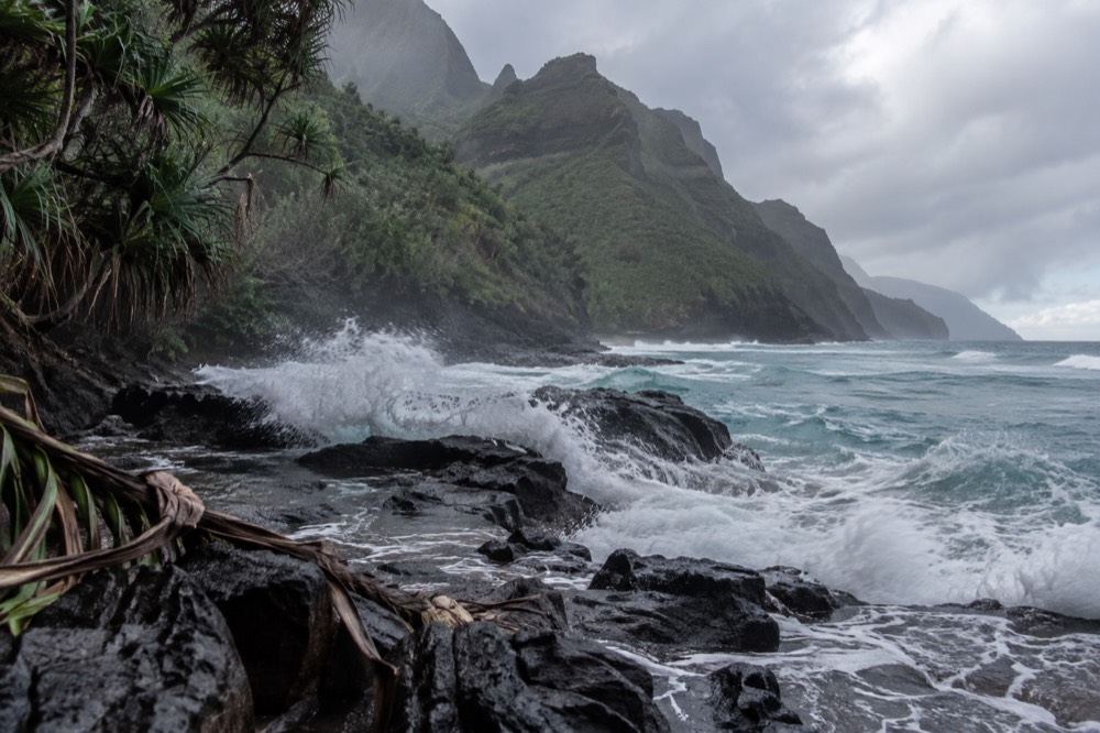 Large waves crashing against a rocky north shore beach with warning signs in the foreground