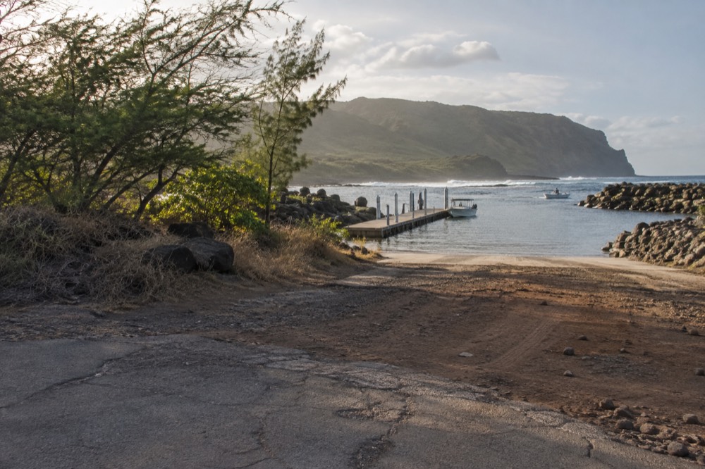 A narrow coastal road ending at a small boat harbor beside dry cliffs on Kauai's west side