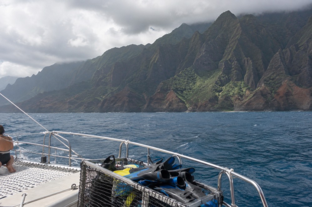 A catamaran deck with snorkel gear stowed and a green cliff coastline in the distance