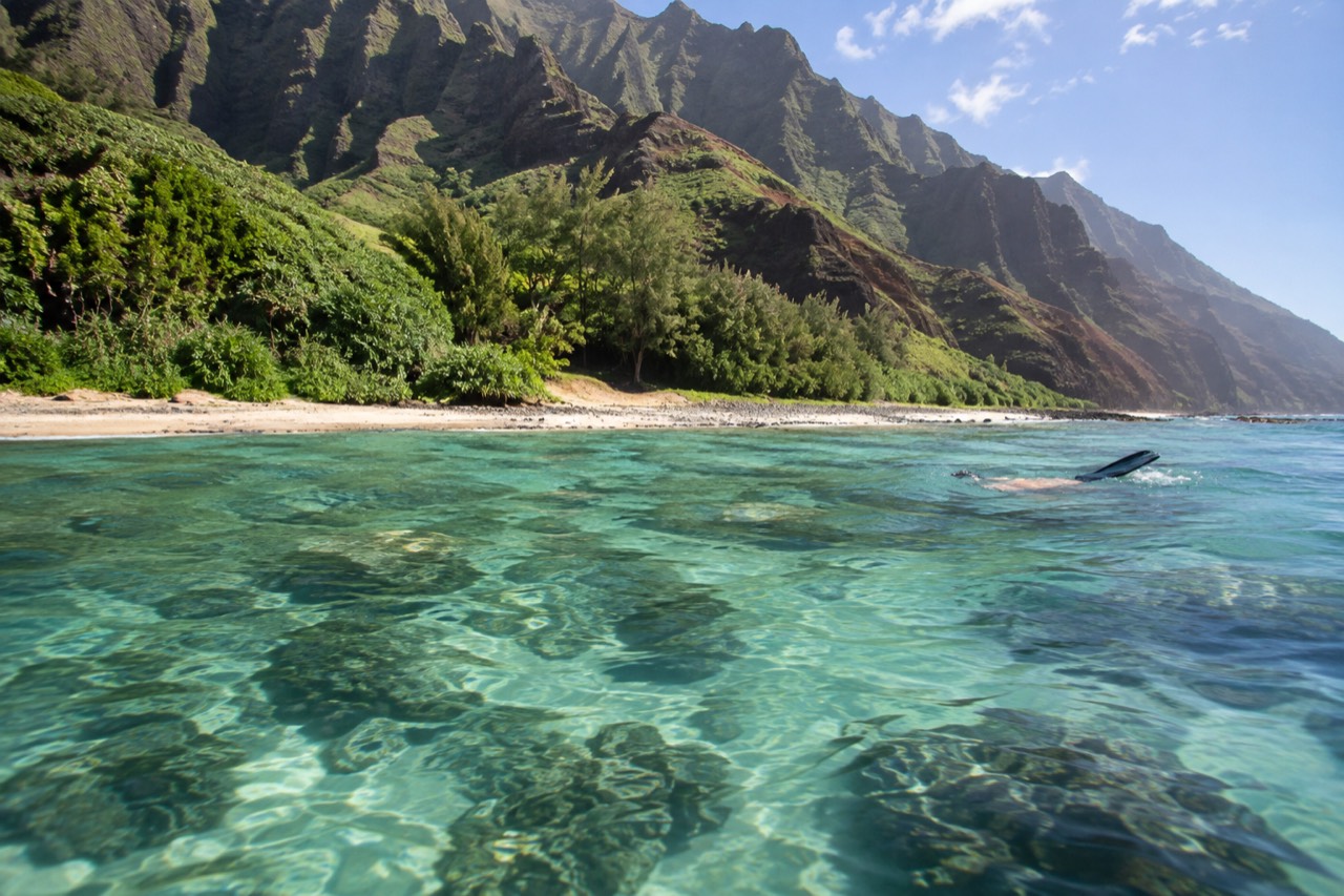 Calm turquoise water over a coral reef along a steep green coastline