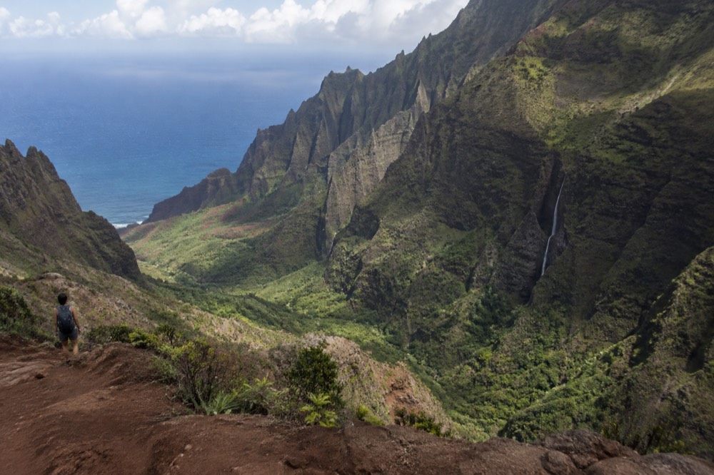 Sea cliffs with narrow green valleys and waterfalls meeting the ocean along a remote coastline