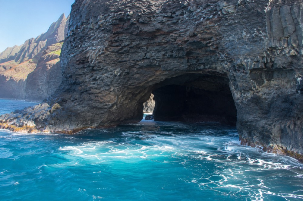 A dark sea cave opening in a cliff face with bright blue ocean water at its mouth