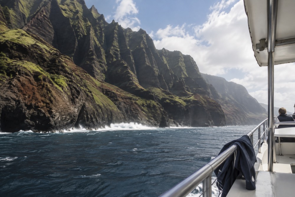 A power catamaran at sea with green cliffs in the background under a partly cloudy sky