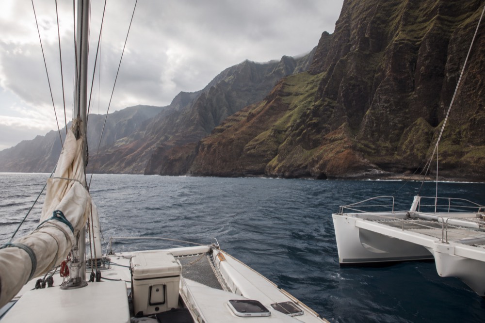 Close alongside two catamaran hulls, one with a furled sail on its mast and one bare-decked on Kauai