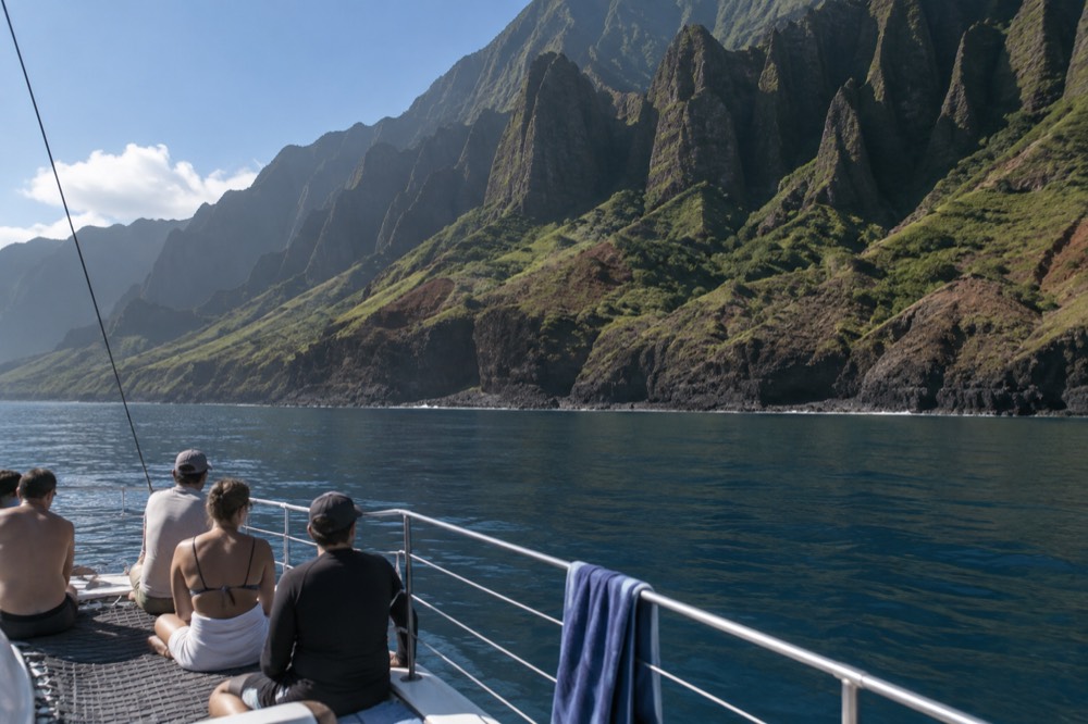 A calm boat passing green Napali sea cliffs under a clear morning sky