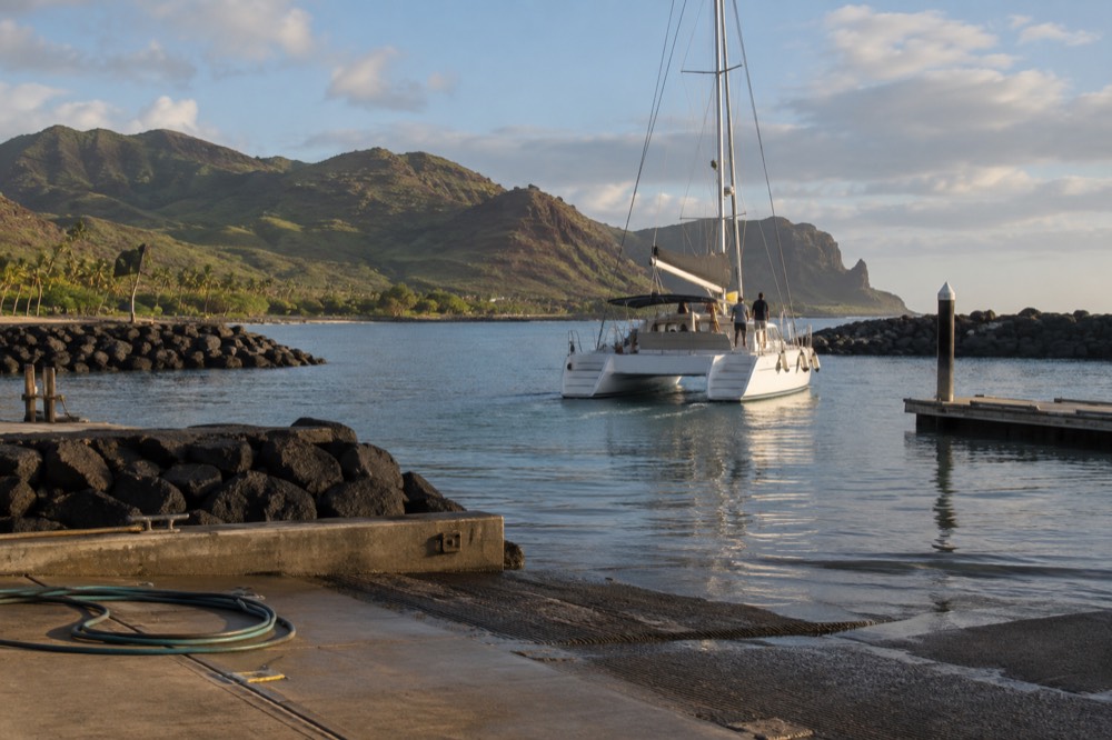 A catamaran cruising past tall sea cliffs on the Napali Coast in flat morning water