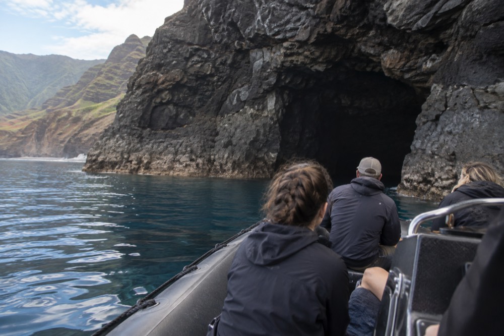 A rigid inflatable raft cruising close to a sea cave entrance in calm water